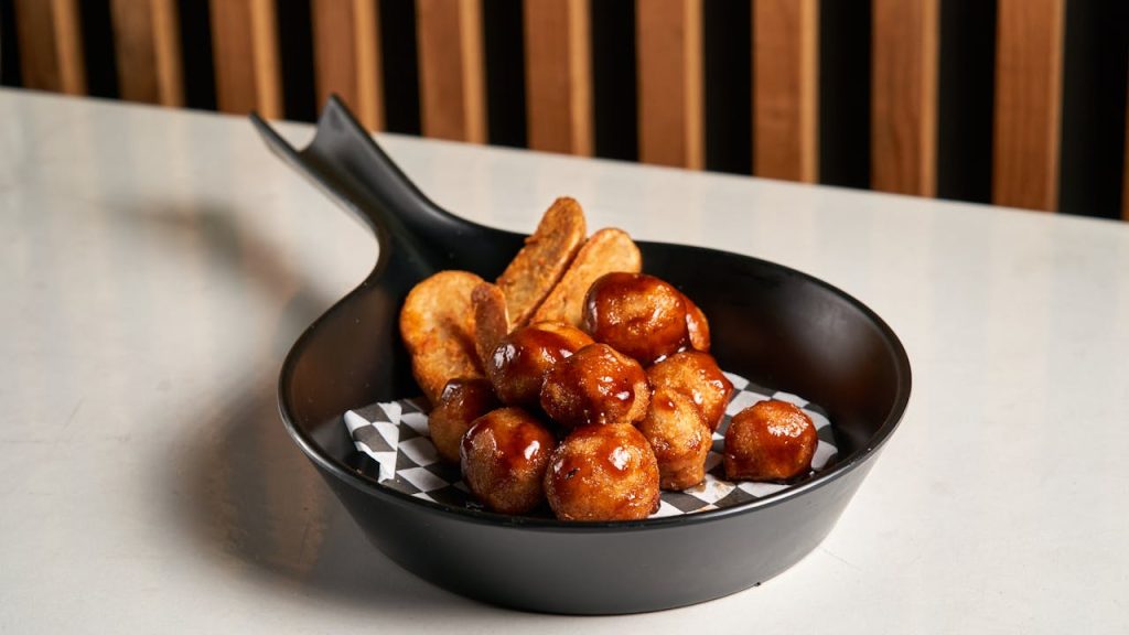 Succulent glazed meatballs with crispy potatoes in a stylish black skillet, perfect for your next gourmet meal.